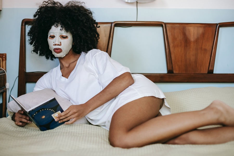 ragazza a letto con maschera facciale che legge un libro